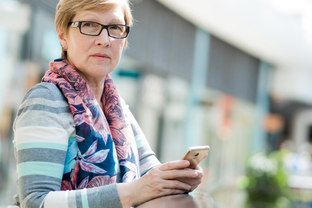 Elegant mature woman uses smartphone, Internet and social networks, portrait at the Mall
