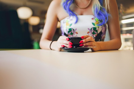 Coffee Cup in hand, a red manicure. Trendy girl with bright colored hairの写真素材