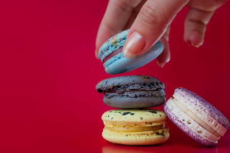 Lot of macarons. Red background. Female hand takes one dessertの写真素材