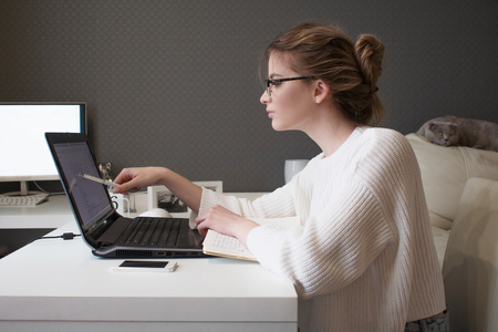 Young businesswoman stares at the screen. Beautiful girl with glasses working at home with laptopの写真素材