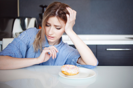 Wants to eat sweet glazed donut. Charming young woman in the kitchen.の写真素材