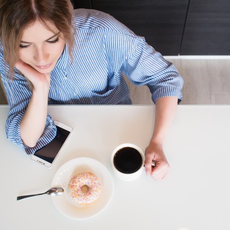 Charming young blonde eat Breakfast at home. Coffee with donut. Top viewの写真素材