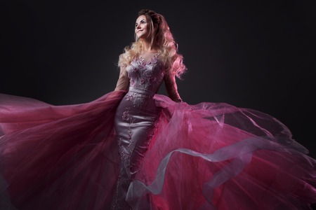 Glamorous lady in a chic pink dress with a train. Studio portrait on gray backgroundの写真素材