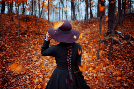 Young stylish girl in coat and hat, background of yellowing leaves, back viewの写真素材