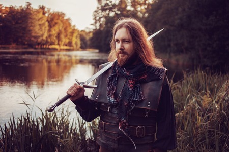 Knight in the forest. A guy in medieval costume with a swordの写真素材