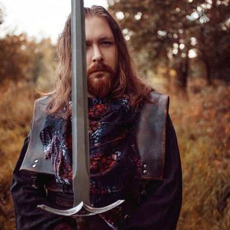 Bearded man knight. A guy in a medieval costume with a swordの写真素材