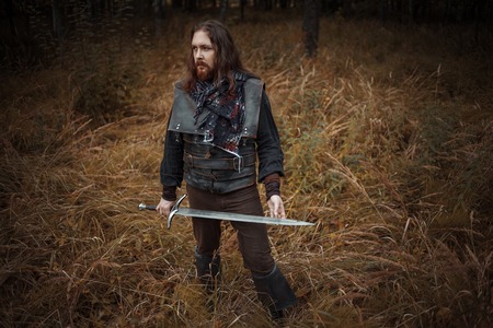 Knight in the forest. A guy in medieval costume with a swordの写真素材