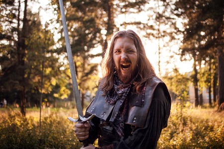 Battle. Knight in the forest. A guy in medieval costume with a sword