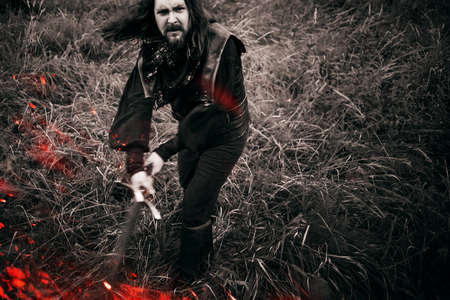 Battle. Knight in the forest. A guy in medieval costume with a sword, effect of fire and toningの写真素材