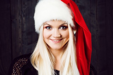 Charming blond woman in Christmas cap. Dark wooden backgroundの写真素材