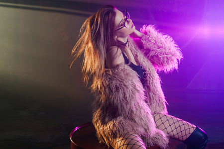 Fashionable young woman in a fluffy pink coat, neon light. Portrait of beautiful trendy girlの写真素材