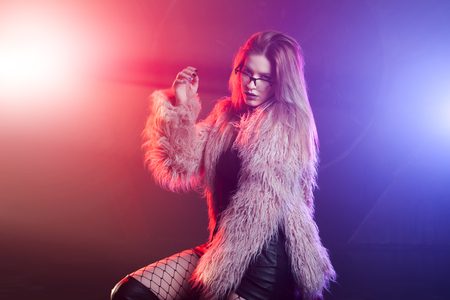 Fashionable young woman in a fluffy pink coat, neon light. Portrait of beautiful trendy girlの写真素材