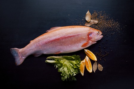 Fresh trout and ingredients to prepare fish dishes on a black tableの写真素材