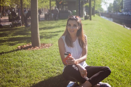Female sitting on the grass drinking coffee in cardboard Cupの写真素材