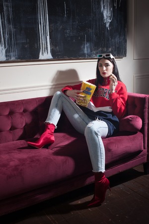 Young woman in a red hoodie, watching movies at home. Eating popcorn.の写真素材