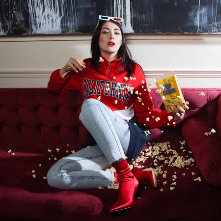 Young woman in a red hoodie, watching movies at home. Eating popcorn.