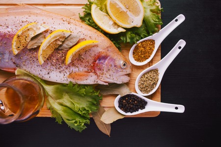 Fresh trout and ingredients to prepare fish dishes on a black tableの写真素材