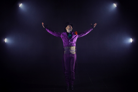 Young man in the purple suit standing on the background of the spotlight. Showman raised hand, show beginsの写真素材