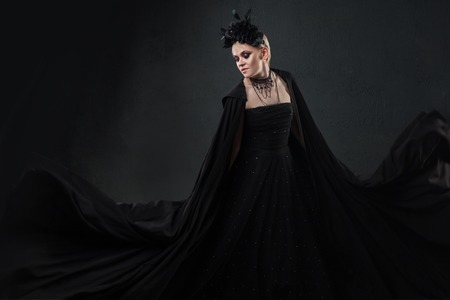 Portrait of an elegant Gothic blonde woman. Girl in a wreath of black flowers and black cloakの写真素材