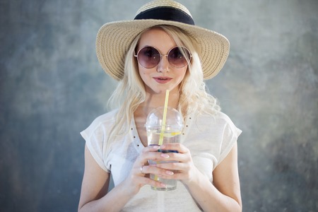 Young beautiful blonde woman in straw hat. Summer style sunglasses. Gray textured backgroundの写真素材