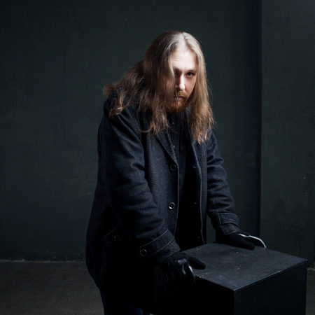 Portrait of a man with long hair and beard in black clothes on dark background