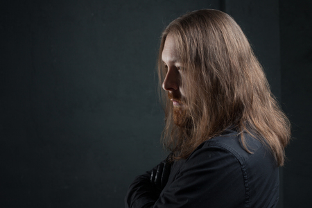 Portrait of a man with long hair and beard in black clothes on dark backgroundの写真素材