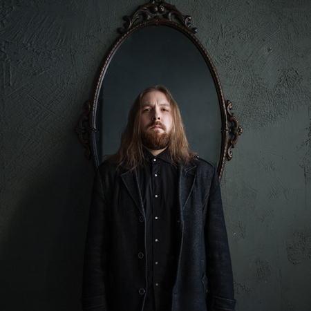 Portrait of a man with long hair and beard in black clothes on the background of mirrorsの写真素材