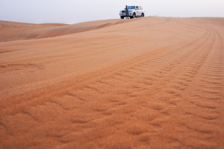 Tire tracks of the SUV in the desert. The car in the distance. Travel to The Arab Emirates