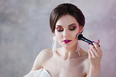 A beautiful young woman is doing herself a makeover. Girl with brush in hand to apply powder on faceの写真素材