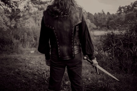 The bearded man knight. A guy in a medieval costume with a sword. Toning, Back view