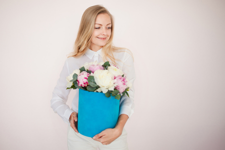 Woman with flowers in a hat box. Bouquet of peonies. Girl in business style, receives flowers or gives, Blue box. free space for textの写真素材
