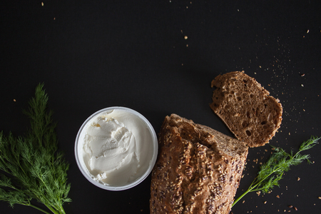 Loaf of multi-grain bread, cut into sandwiches. And cream cheese. Close-up, free space for text. Black backgroundの写真素材