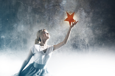 Young attractive woman reaching for the star. Take a star from the sky, dreams and plans, concept. Textured gray backgroundの写真素材