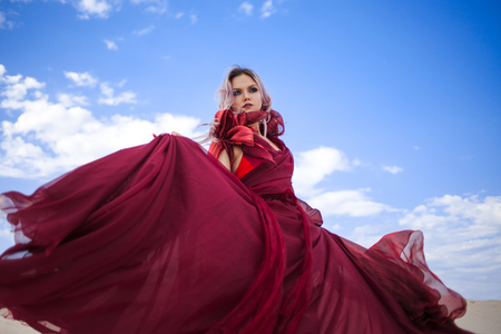 Girl in red. Beautiful young woman in a scarlet dress flying. Outdoors, against the skyの写真素材