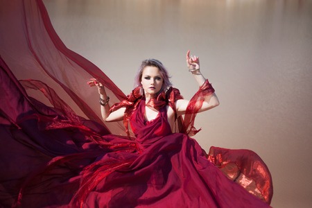 Lady in red. Young beautiful woman in red flying dress. Outdoors, in the desertの写真素材