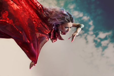 Fantastic nymph flies. Fabulous portrait of a flying woman in a red dress. Fall downの写真素材