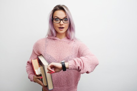 Time to learn. Student. Young woman with books. Student girl with a stack of books, looking at the clock and surprisedの写真素材