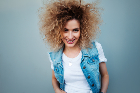 Young attractive woman with very lush hair. Portrait of a beautiful cute girl in a denim vestの写真素材