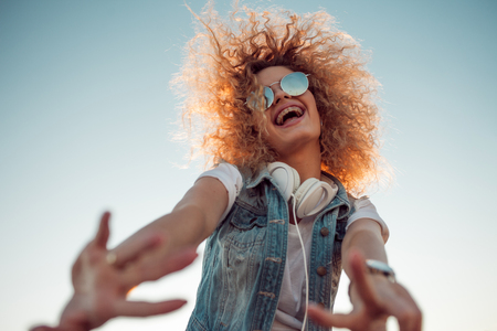 Young stylish woman with very lush hair makes a friendly gesture. Young woman with big headphones. outdoors portrait of a trendy girlの写真素材