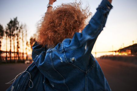 Walking on the street, trendy young woman with lush hair go ahead. Back view. Hand upの写真素材