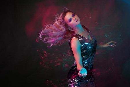 Bright and stylish young woman dancing in club, color light, motion effects. Black background, long...