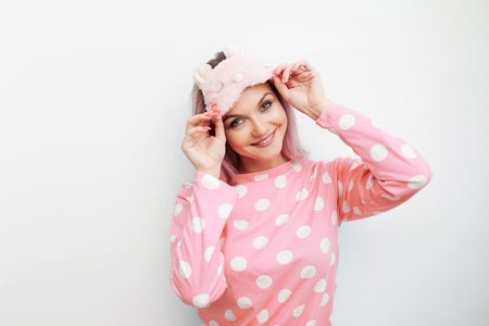 Beautiful young blonde in pink pajamas and a sleep mask. girl woke up in the morning, concept of cheerful beginning of dayの写真素材