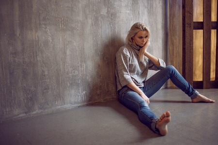 Depressed woman. blonde girl sitting on the floor, sadness and depression, concept of psychological problemの写真素材