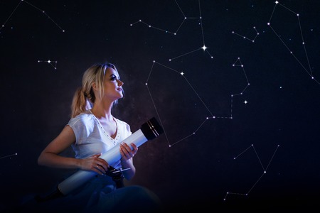 young woman with a telescope in her hands on the background of the starry sky. Concept, science and research. Dreams and goalsの写真素材