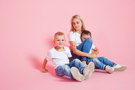 happy mom with two happy sons. Young woman and two baby boys, pink backgroundの写真素材