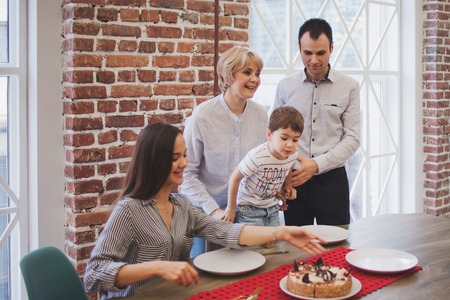 Family dinner. Family receives guests, a festive meeting. family serves table and communicates with each other. Parents children and grandchildren in the house, cake on table.の写真素材