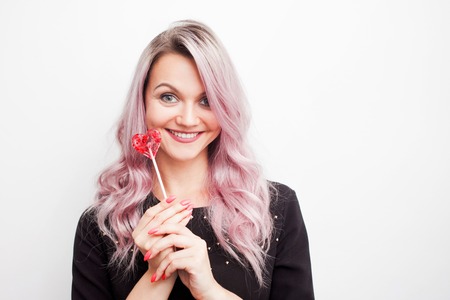 Lovely charming girl with a Lollipop in the form of heart. Portrait of a young woman with pink hair and pink candy, concept Valentine's dayの写真素材
