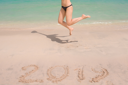 New 2019 year in the South, the sea. Sea surf. Blue wave is coming ashore. Inscription on sand and women's legs, celebrate new year in the tropics. New year holidaysの写真素材