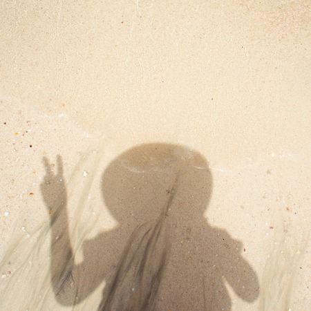 texture of wet sand, surf. Women's shadow on the sand, the girl in the hat shows the gesture of two fingers,の写真素材