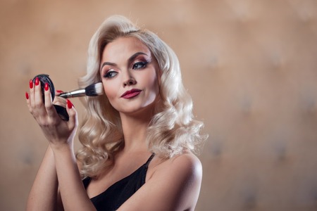 Beautiful young blonde makes a bright holiday makeup. Glamorous make-up. An attractive young woman paints the eyelashesの写真素材